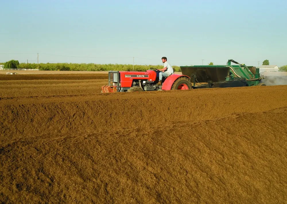 Hileras de compost en una granja con un tractor volteándolas